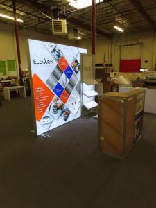 Modified ECO-1070 Sustainable Exhibit with Aluminum Extrusion Frame, Backlit Tension Fabric Graphic, Modifed ECO-35C Counter with Locking Storage, (3) Angled Product Shelves, and Monitor Mount  -- View 2